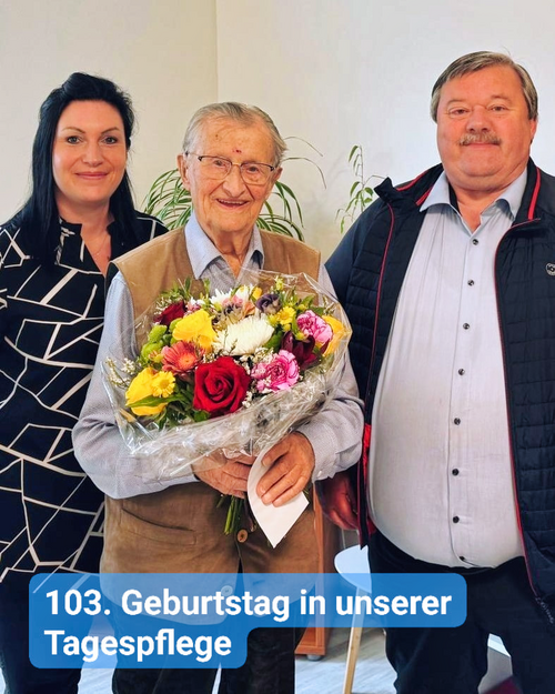 Eine Frau und ein Mann überreichen einem Senior zum 103. Geburtstag einen großen Blumenstrauß
