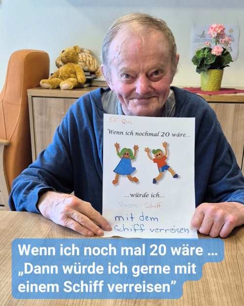 Ein älterer Herr sitzt an einem Holztisch, und er hält lächelnd ein Papier in die Kamera. Bildbeschriftung: Wenn ich noch mal 20 wäre … „Dann würde ich gerne mit einem Schiff verreisen”