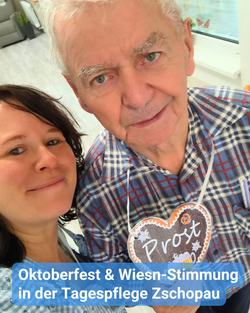 Betreuungskraft und Senior lächeln in die Kamera. Der Senior hat ein Lebkuchenherz um den Hals gehängt. Bildbeschriftung: Oktoberfest & Wiesn-Stimmung in der Tagespflege Zschopau