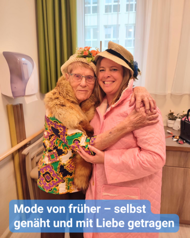 Eine ältere Dame und eine jüngere Frau lächeln in die Kamera, während sie sich umarmen. Sie präsentieren bunte Mode. Bildbeschriftung: Mode von früher – selbst genäht und mit Liebe getragen