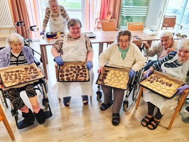 Sechs Seniorinnen sind gemeinsam am Plätzchenbacken und zeigen ganz stolz vier Backbleche voller Weihnachtsplätzchen