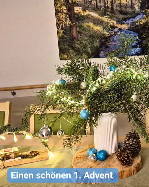 Weihnachtliche Tischdekoration mit Schwibbogen, Adventsstrauß, Lichterkette und Zapfen. Bildbeschriftung: Einen schönen 1. Advent 