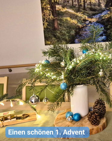 Weihnachtliche Tischdekoration mit Schwibbogen, Adventsstrauß, Lichterkette und Zapfen. Bildbeschriftung: Einen schönen 1. Advent 