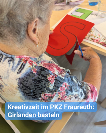 Eine betagte Dame schneidet mit einer Schere ein rotes „S“ aus Papier, während sie Girlanden fertigt.