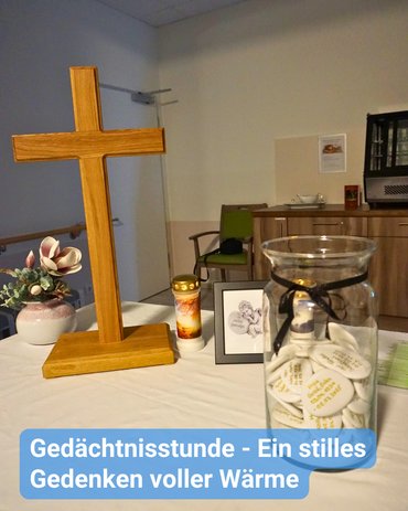 Holzkreuz, Gedenkkerze und ein Glas mit beschrifteten Erinnerungssteinen auf einem weißen Tisch während der Gedächtnisstunde in der Seniorenresidenz Kamelienhof; symbolischer Aufbau für stilles Gedenken und gemeinsame Erinnerungskultur.