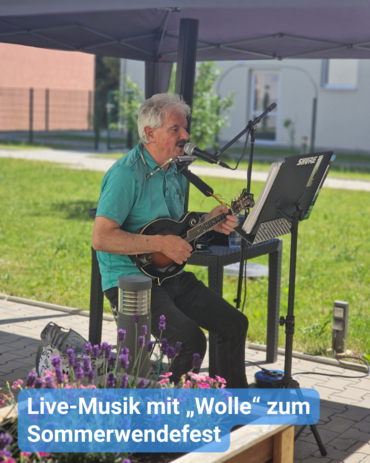 Ein Mann spielt Mandoline und Mundharmonika unter einem Pavillon. Text: 'Live-Musik mit „Wolle“ zum Sommerwendefest'.