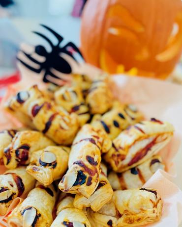 Gruselig leckere Halloween-Snacks in der Tagespflege Fraureuth – Würstchen im Blätterteig und dekorative Spinne vor geschnitztem Kürbis im Pflegekompetenzzentrum Fraureuth.