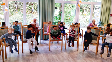 Kindergartenkinder und Seniorinnen sitzen im Kreis und musizieren gemeinsam.