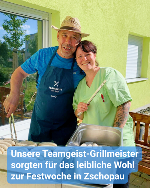 Zwei Personen grillen Würstchen: Ein Mann mittleren Alters, gekleidet in einen Strohhut und eine blaue Schürze mit dem Aufdruck „TEAMGEIST am Grill“, steht in enger Nähe zu einer Frau. Der Mann hat seinen Arm um die Schultern der Frau gelegt. Sie trägt einen hellen grünen medizinischen Kittel.  Beide befinden sich vor einer leuchtend gelben Wand mit einem seitlich gelegenen Fenster.  Sie stehen hinter einem mit Würstchen beladenen Grill.  Über dem Bild ist der Text „Unsere Teamgeist-Grillmeister sorgten für das leibliche Wohl zur Festwoche in Zschopau“ eingeblendet.