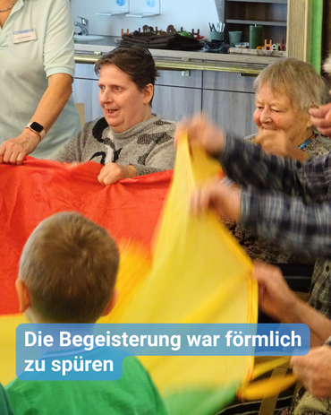 Nahaufnahme von Kindern und Senioren am Schwungtuch. Die Augen der Bewohner leuchten, und sie haben ein Lächeln auf dem Gesicht. Bildbeschriftung: Die Begeisterung war förmlich zu spüren