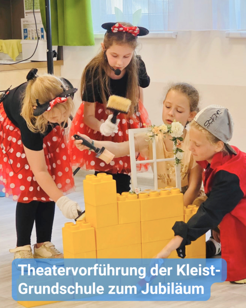 Vier Kinder in Kostümen bauen mit großen gelben Bausteinen. Text: 'Theatervorführung der Kleist-Grundschule zum Jubiläum'.