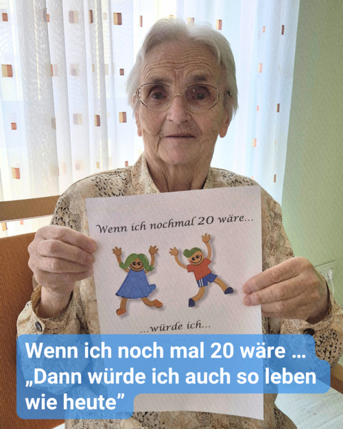 Eine ältere Dame sitzt vor einem Fenster mit hellen Gardinen und hält einen Zettel in die Kamera. Bildbeschriftung: Wenn ich noch mal 20 wäre … „Dann würde ich auch so leben wie heute”