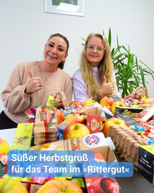 Zwei Kolleginnen bereiten für Ihr Team eine süße Überraschung vor: auf dem Tisch sind Süßigkeiten, Getränke sowie Obst zu finden. Bildbeschriftung: “Süßer Herbstgruß für das Team im »Rittergut«