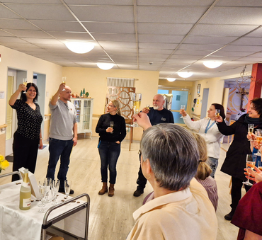  Mitarbeiterinnen und Mitarbeiter stehen im Kreis und verabschieden sich mit einem Glas Sekt von einem Kollegen