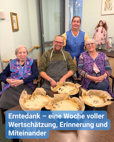 Zwei Seniorinnen und zwei Betreuungskräfte – alle tragen Schürzen – sitzen vor einem Tisch mit vier Kuchenformen. Stolz präsentieren sie den selbstgemachten Pflaumenkuchen. Bildbeschriftung: „Erntedank – eine Woche voller Wertschätzung, Erinnerung und Miteinander“