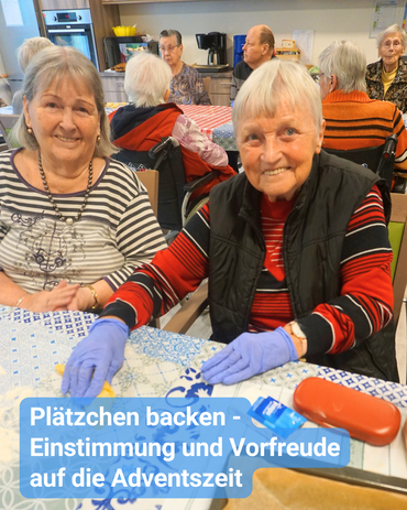 In einer Gemeinschaftsküche sind Seniorinnen und Senioren gemeinsam am Backen. Im Vordergrund sind zwei Seniorinnen, die in die Kamera lächeln und Teig zubereiten. Bildbeschriftung: „Plätzchen backen – Einstimmung und Vorfreude auf die Adventszeit“