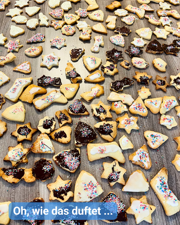 Ein Tisch voll mit verschiedenster Weihnachtsplätzchen, ob mit dunkler Schokoladenglasur oder bunten Zuckerstreuseln dekoriert. Bildbeschriftung: “Oh, wie das duftet …”
