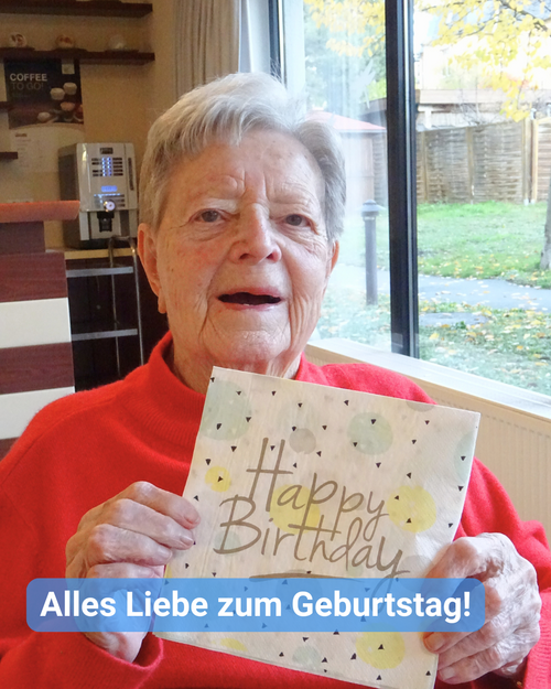Seniorin im roten Pullover, hält eine Serviette mit Happy Birthday in die Kamera. Bildbeschriftung: Alles Liebe zum Geburtstag!