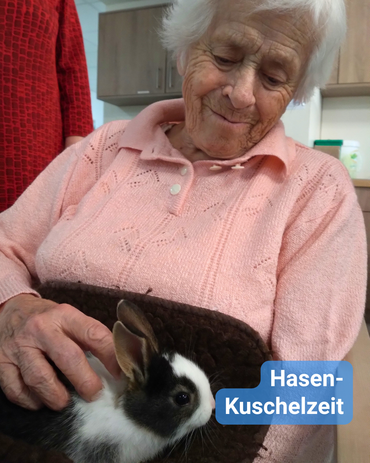 Seniorin im rosa Pullover hat einen Hasen auf dem Schoß und streichelt ihn. Bildbeschriftung: „Hasen-Kuschelzeit“