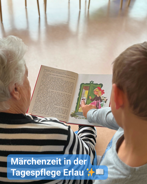 Eine Seniorin liest aus einem Märchenbuch vor. Ein Kind steht neben ihr und zeigt mit dem Finger auf die Buchillustration. Bildbeschriftung: „Märchenzeit in der Tagespflege Erlau“