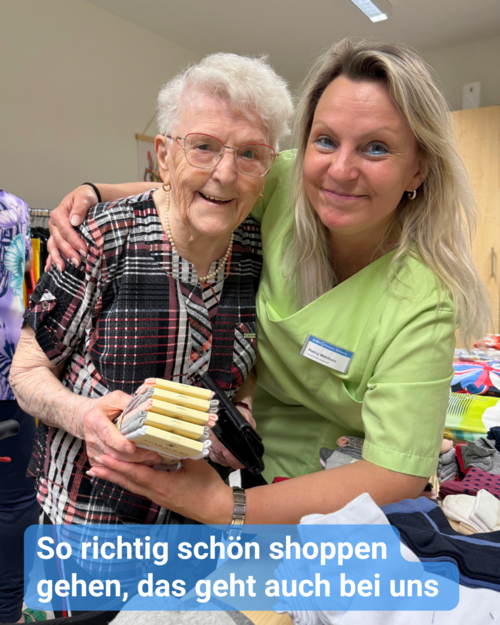 Seniorin und Betreuerin lächeln in die Kamera. Beide haben Freude beim Textileinkauf. Bildbeschriftung: So richtig schön shoppen gehen, das geht auch bei uns
