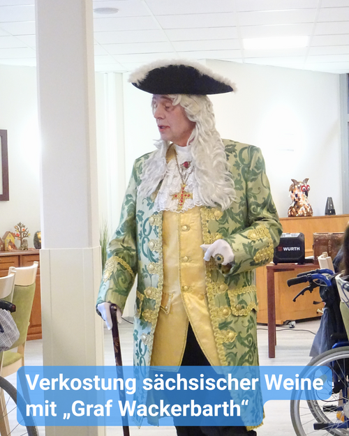 Ein kostümierter Mann in der traditionellen Kleidung der Hofgesellschaft des frühen 18. Jahrhunderts. In Gold- und Grüntönen, mit Seide und Spitze. Mit einem goldenen Kreuz als Kette sowie einem schwarzen Hut. Bildbeschriftung: Verkostung sächsischer Weine mit „Graf Wackerbarth“